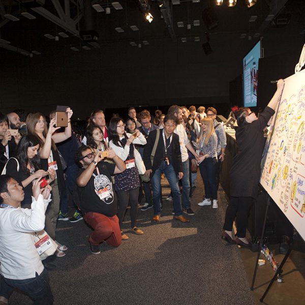 imagethink graphic recorder yao xiao completes a title at the top of a board at SXSWi while attendees photograph the content that was created during the session.