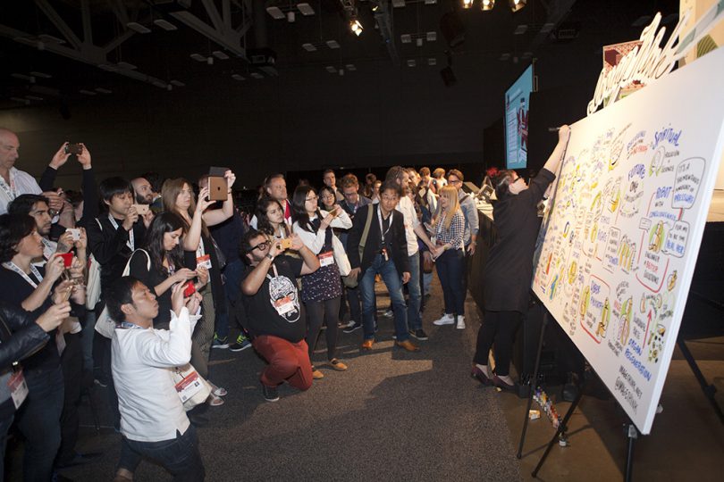 imagethink graphic recorder yao xiao completes a title at the top of a board at SXSWi while attendees photograph the content that was created during the session.