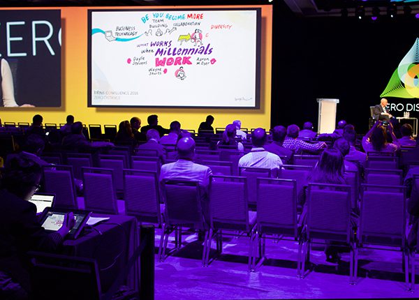 Image of conference hall and attendees onlooking speakers and projected ImageThink boards.