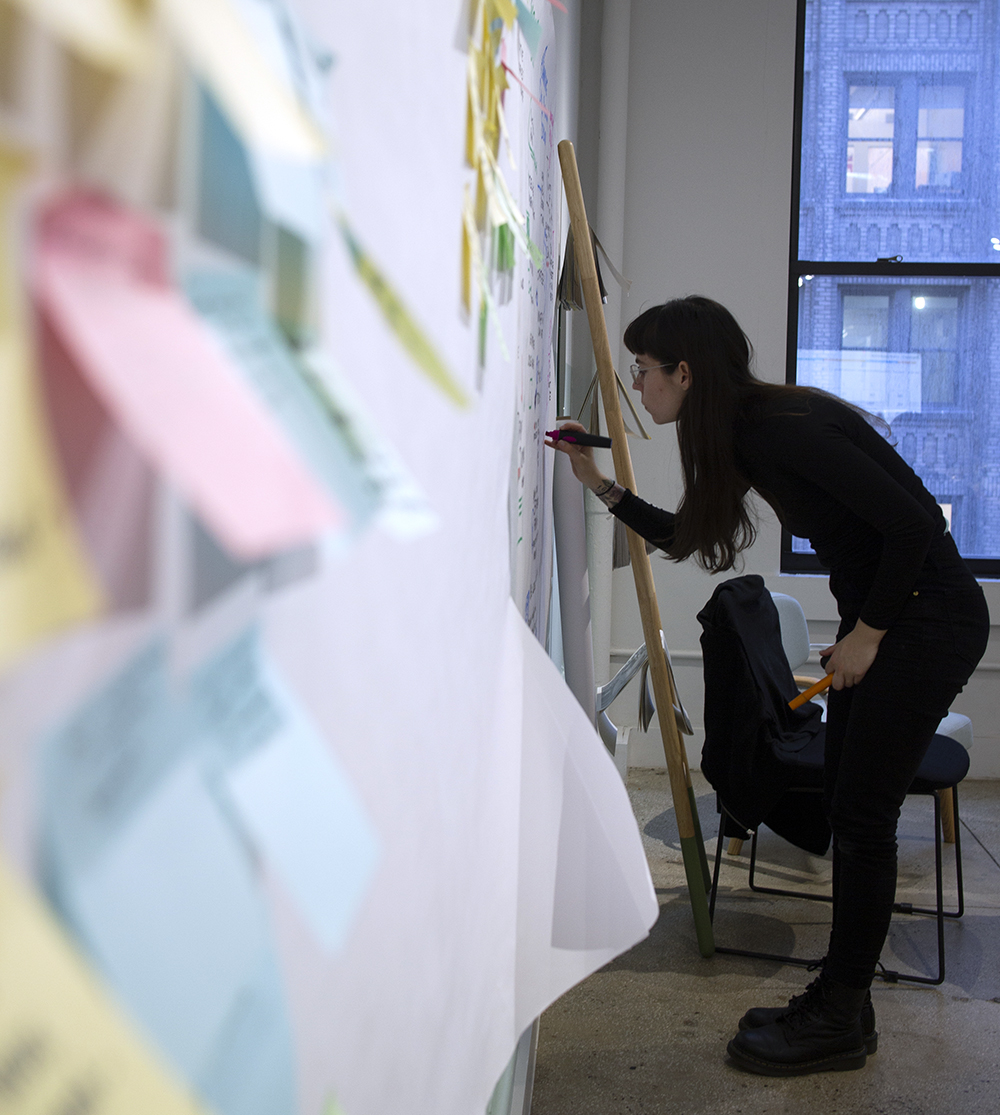 Ona Rygelis, graphic recorder of ImageThink, scribes on a whiteboard with post it notes.
