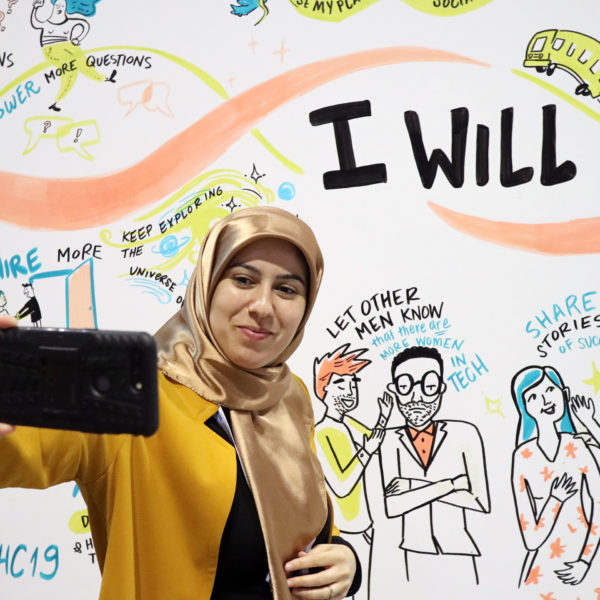 Attendee at the 2019 Grace Hopper Celebration taking a selfie with one of our Social Listening Murals at the Anita B. Booth.