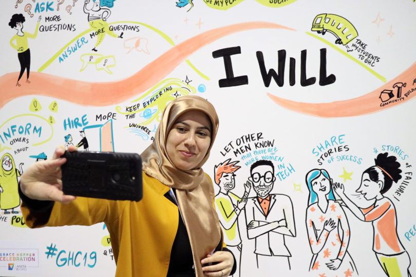 Attendee at the 2019 Grace Hopper Celebration taking a selfie with one of our Social Listening Murals at the Anita B. Booth.