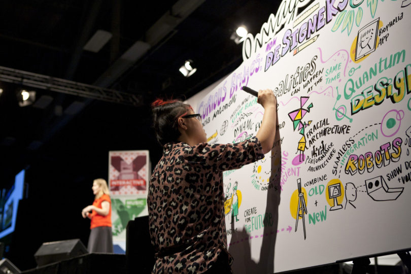 ImageThink scribe in the foreground shown graphic recording for a SXSW keynote speaker on stage