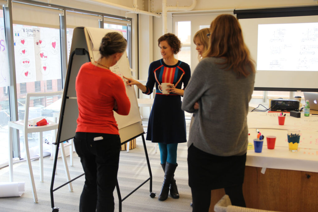 ImageThink CEO Nora Herting speaking with others while pointing to an easel in an office