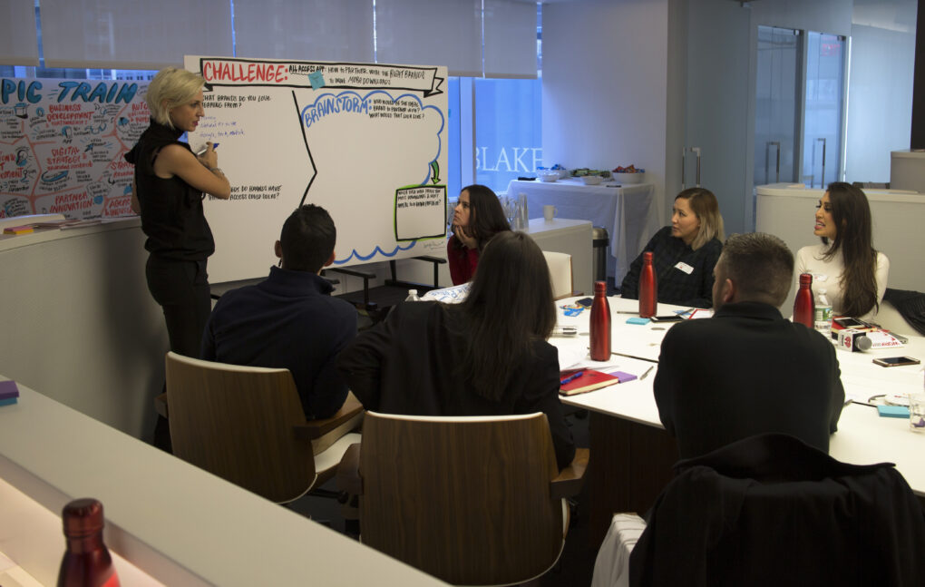 A graphic facilitator refers to an illustrated board while speaking to meeting attendees.