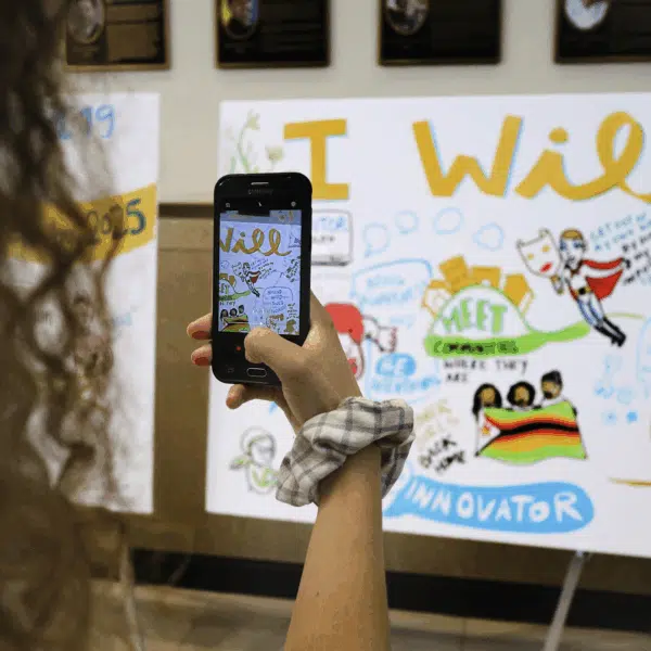 A nonprofit attendee photographs a colorful commitment mural with her phone.