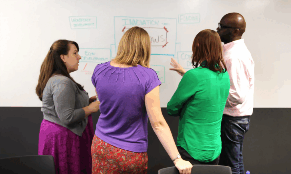 Team gathers at a whiteboard, using visual note taking to align on strategy and goals.