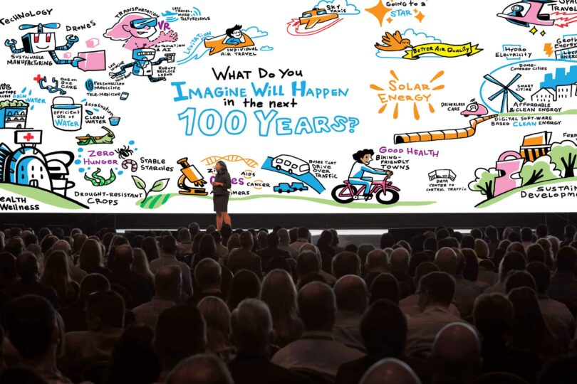 Live conference keynote with graphic recording visuals projected behind the speaker.